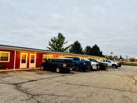 Una fila de vehículos recreativos estacionados en un estacionamiento, con un edificio rojo al fondo.