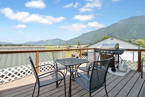 A deck with a grill, chairs, and a table overlooking a mountainous landscape.