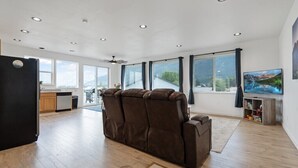 Un salón amplio con un sofá reclinable grande, una zona de cocina y un televisor en la pared.