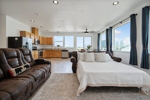 A modern bedroom with a large bed, a leather sofa, and a view of the city through large windows.