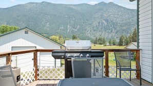 Una terraza con una parrilla, sillas y vistas a montañas.