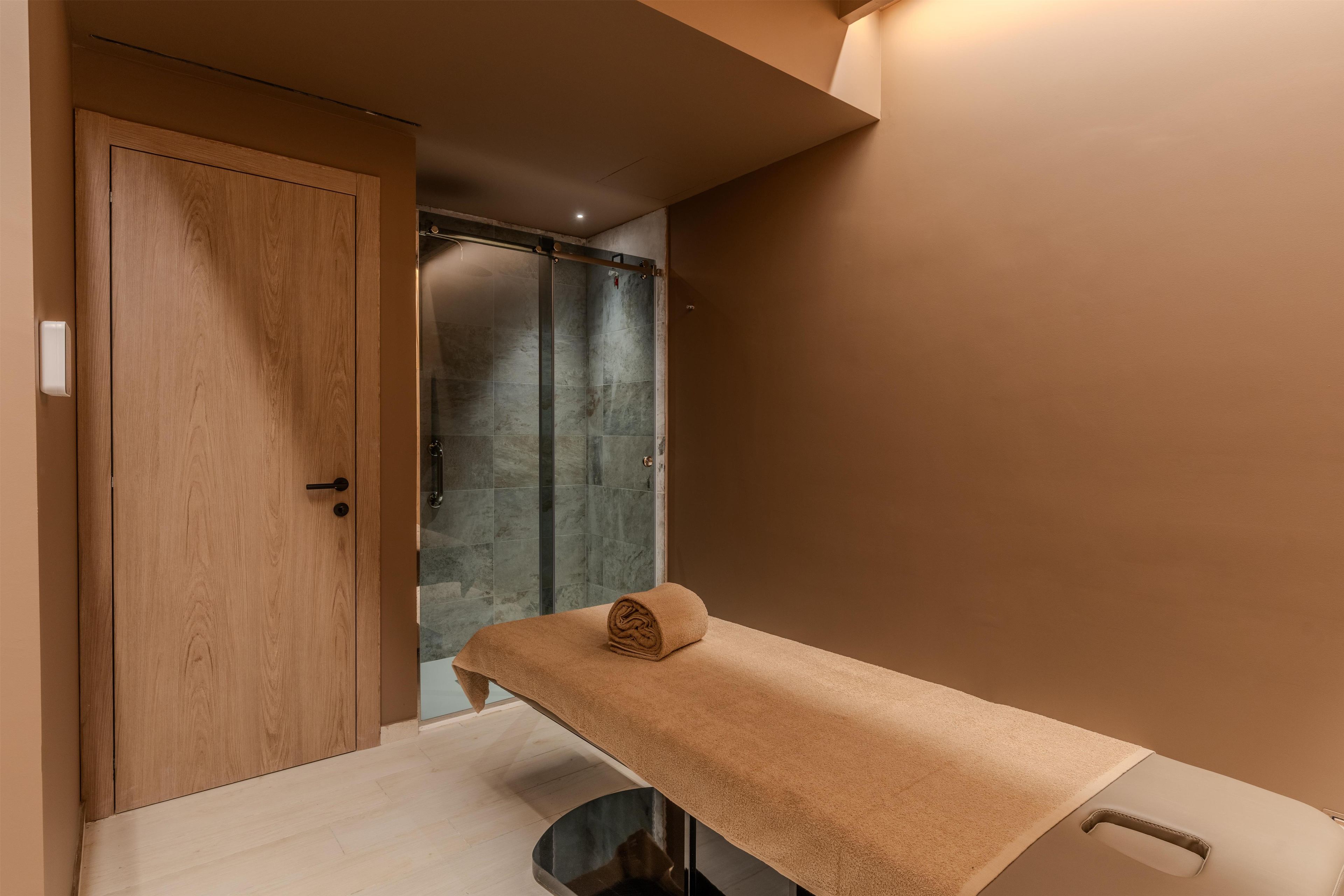 Een kamer met een houten deur, een glazen douchecabine en een massagetafel met een handdoek.