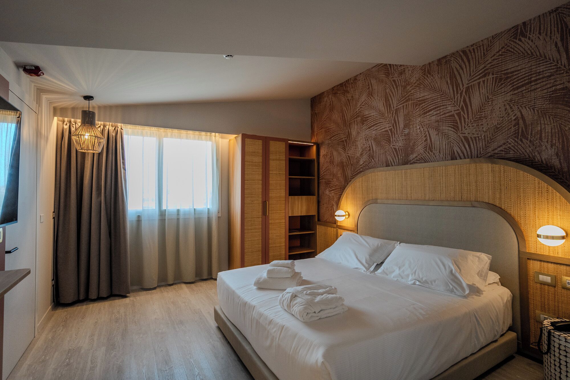 Een hotelkamer met een bed, een kledingkast, een nachtkastje en een raam met gordijnen.