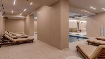 Un espace piscine intérieur moderne, doté de chaises longues et d’une table de billard.