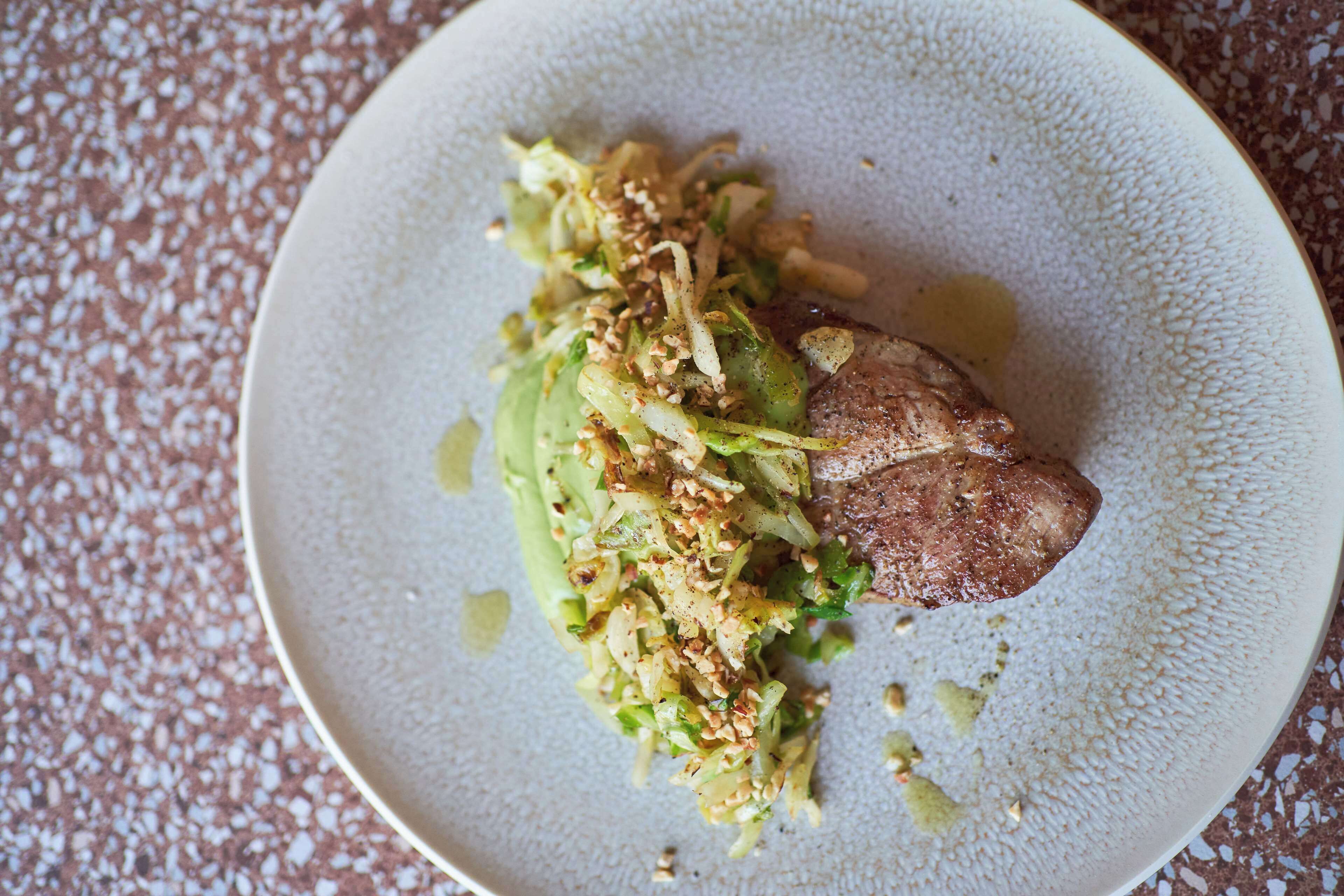 A plate with a piece of meat and a green vegetable salad.