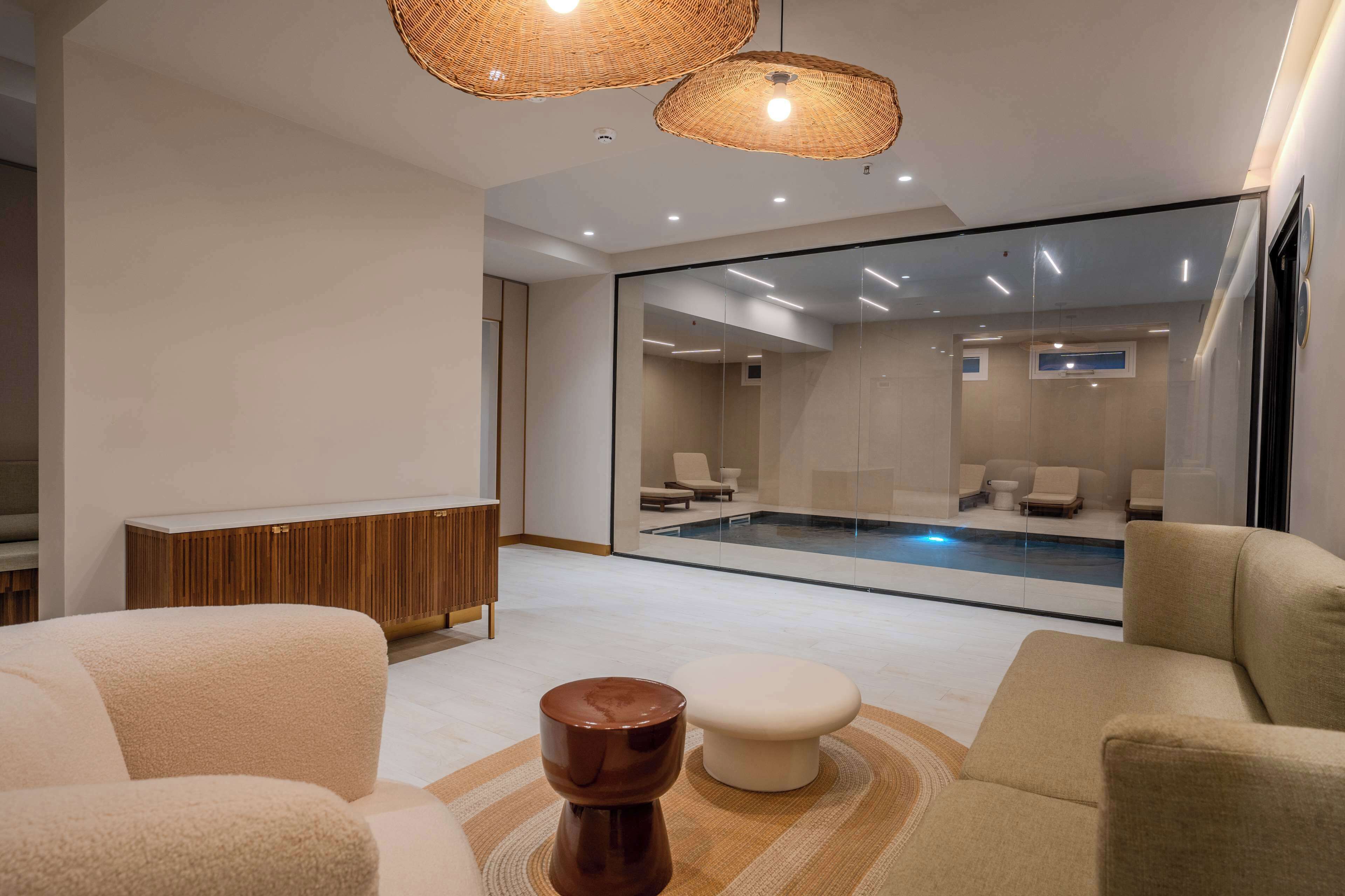 Un moderno spa con pared de vidrio, piscina y zona de estar con sofá y reposapiés.
