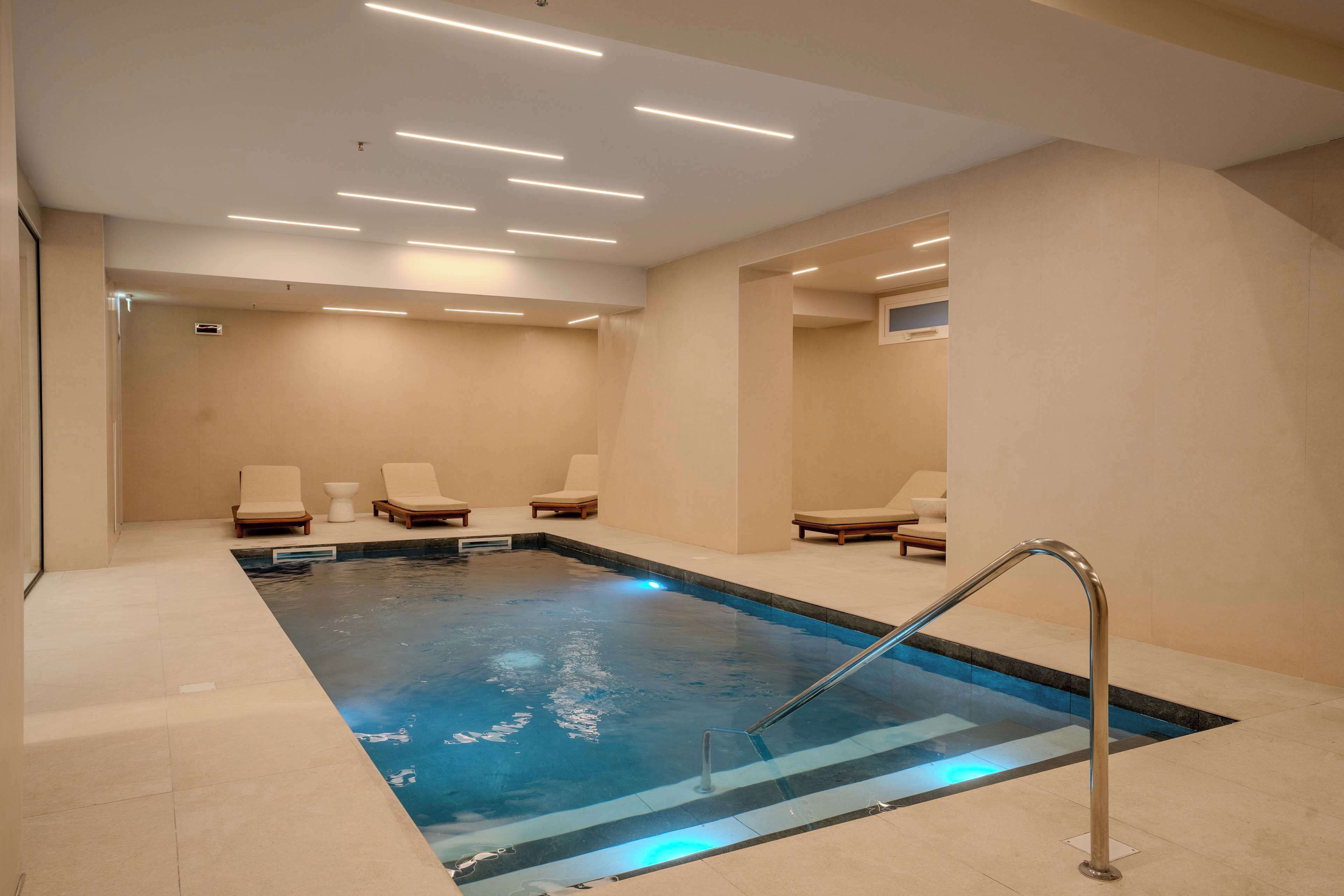 A spa area with a pool, lounge chairs, and a modern ceiling design.