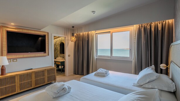 A hotel room with two beds, a TV, a bathroom, and a view of the sea. - Terradamari Resort & Spa Marina di Modica, Tapestry by Hilton (Modica)