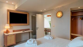 Habitación de hotel con cama, escritorio, espejo, armario y baño visible a través de una puerta abierta.