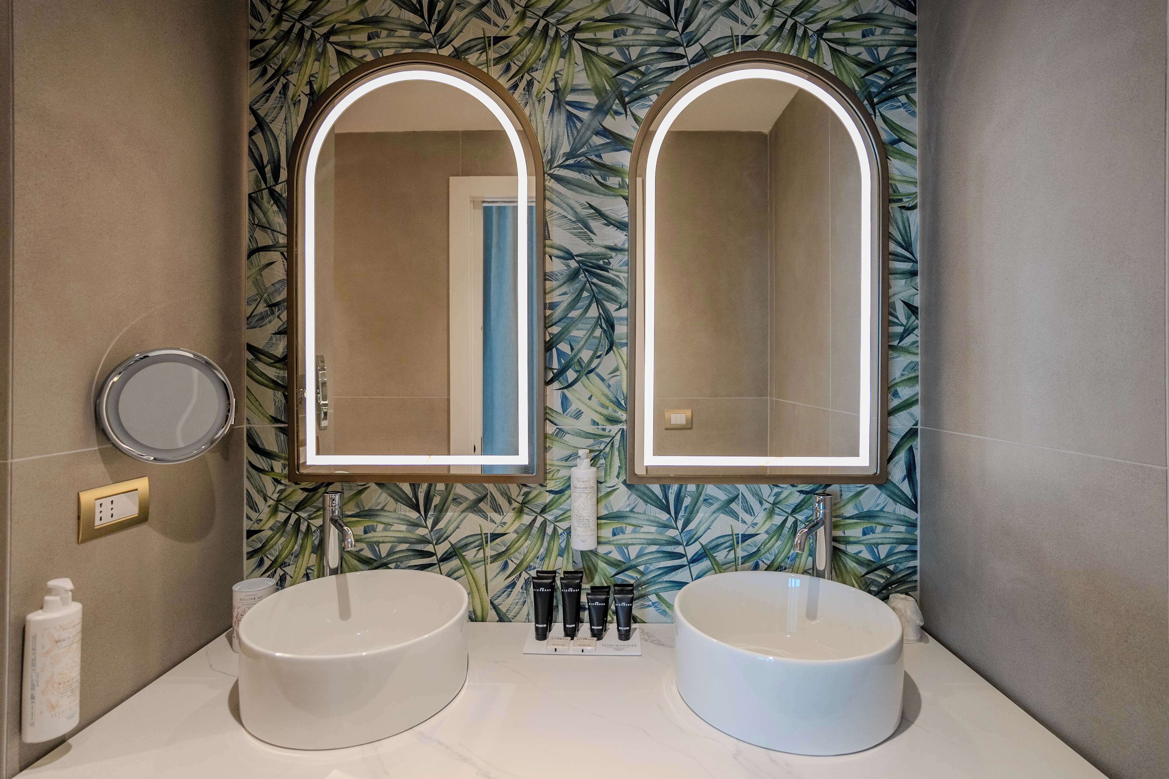 A bathroom with two sinks, a mirror, and a wall with a leaf pattern.