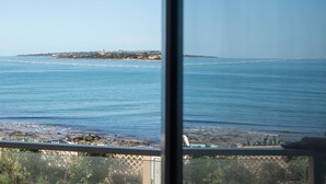 A coastal view from a window, featuring a beach, ocean, and a distant island with buildings. - Terradamari Resort & Spa Marina di Modica, Tapestry by Hilton (Modica)