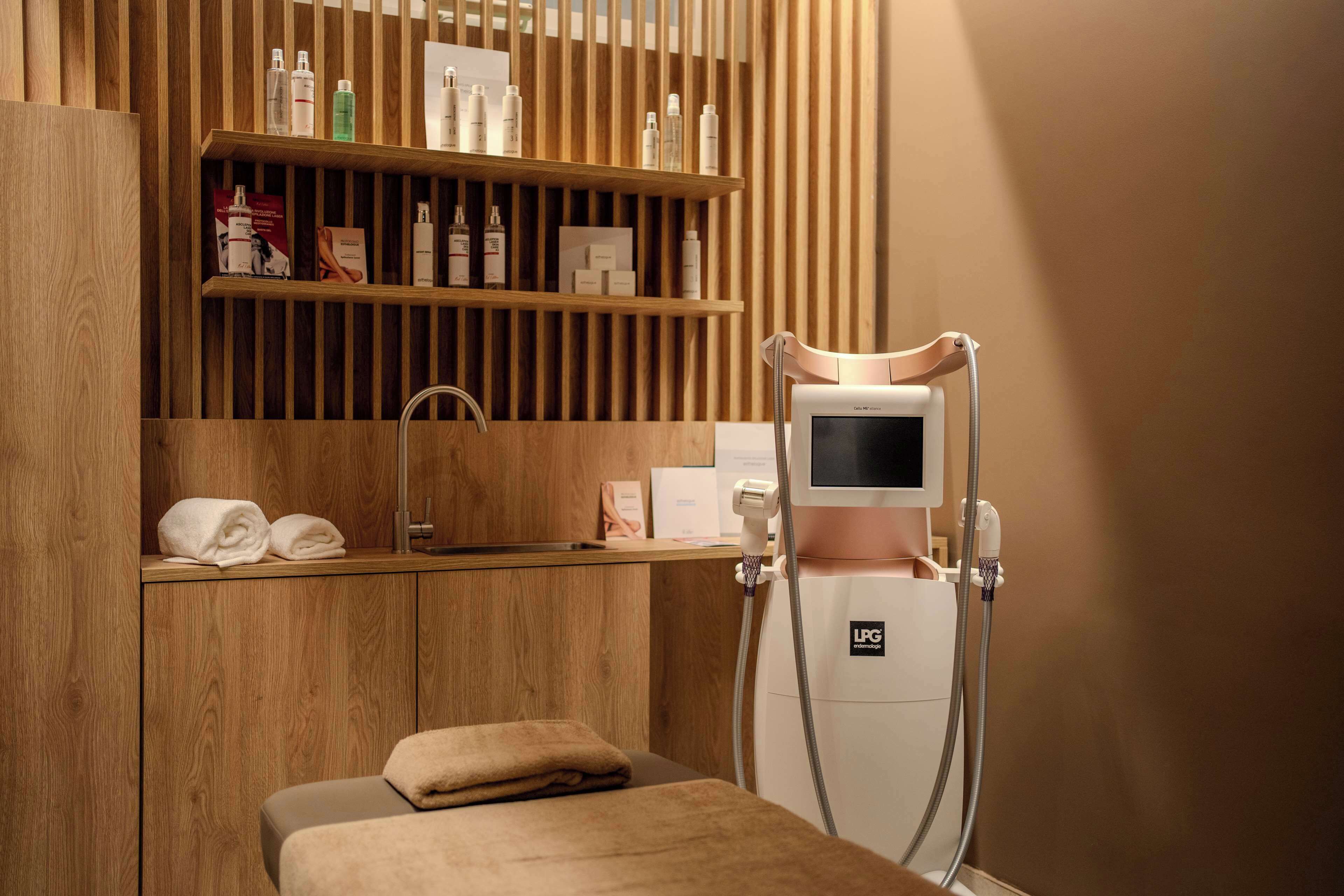 A spa room with a wooden vanity, shelves with toiletries, a massage table, and a LCG device.