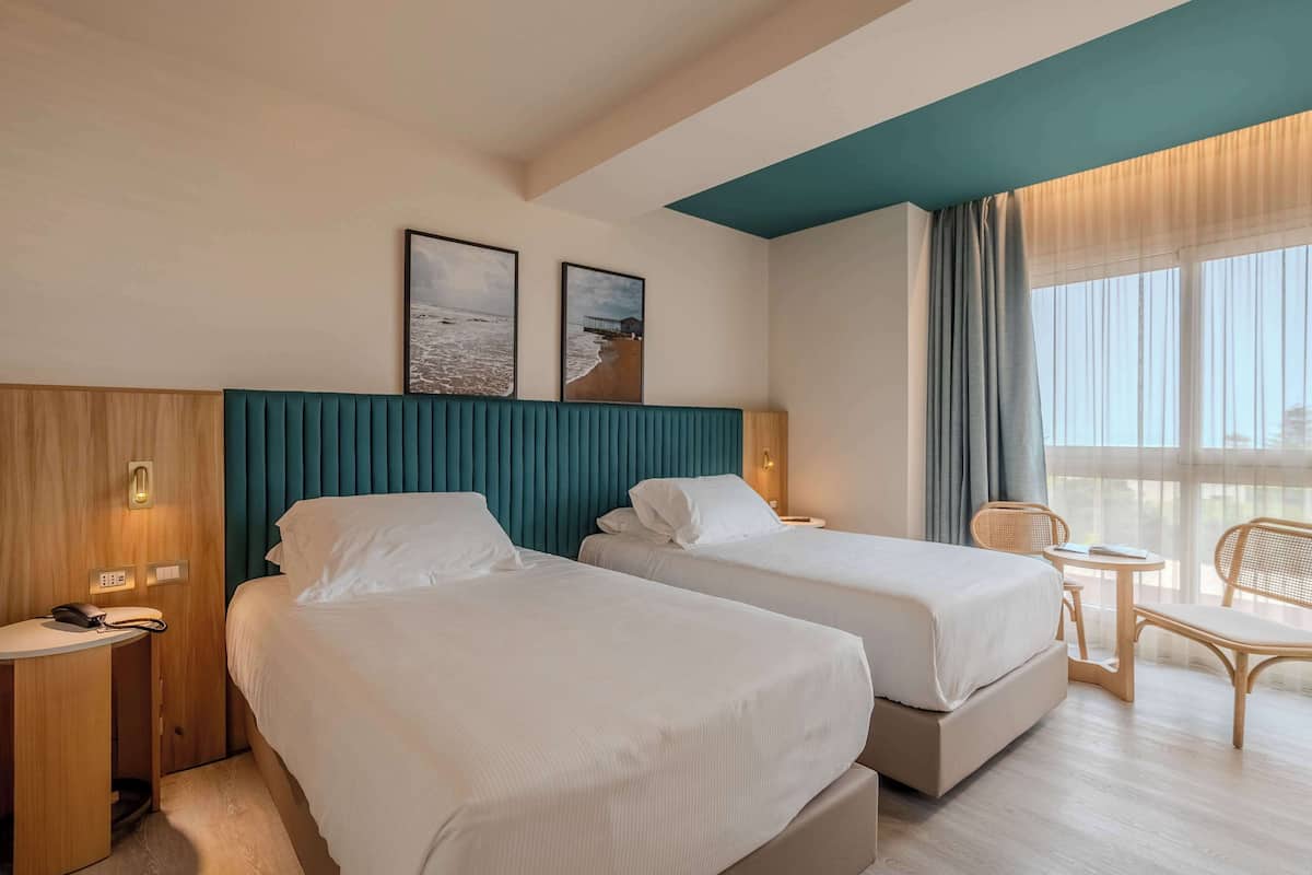A hotel room with two beds, a desk, a chair, and a small table.