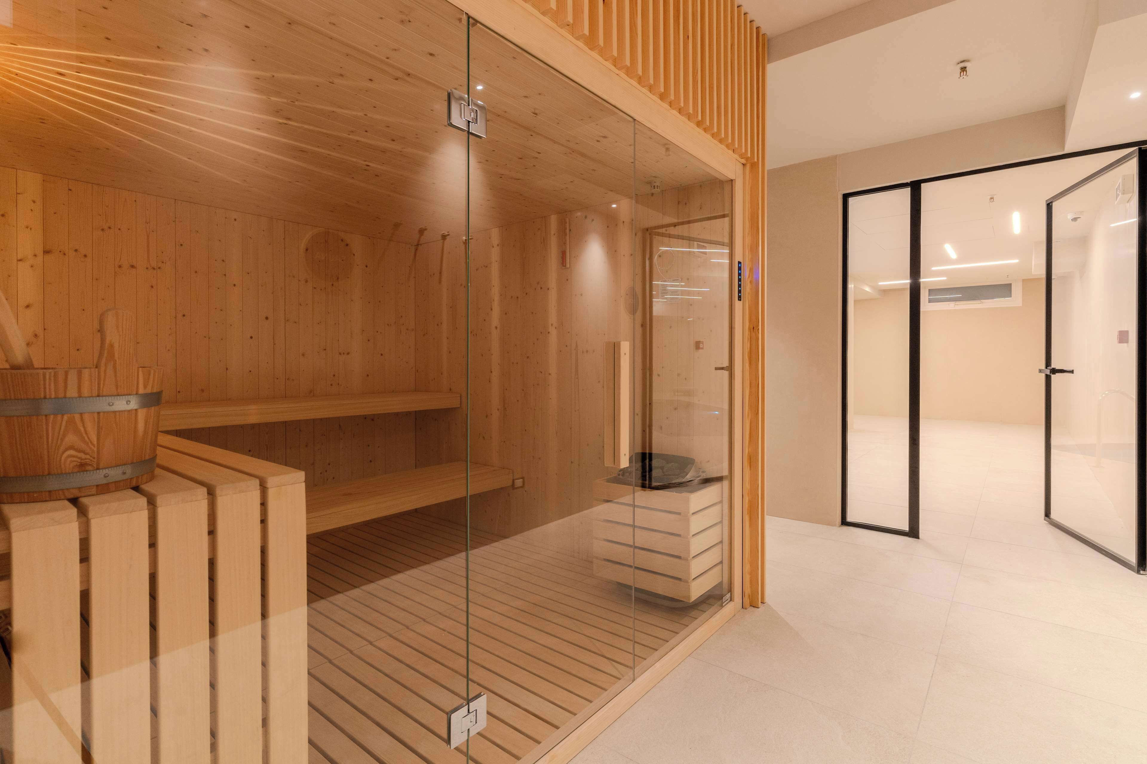 Een sauna met houten wanden en een glazen deur, een houten bank en een klein houten kastje.