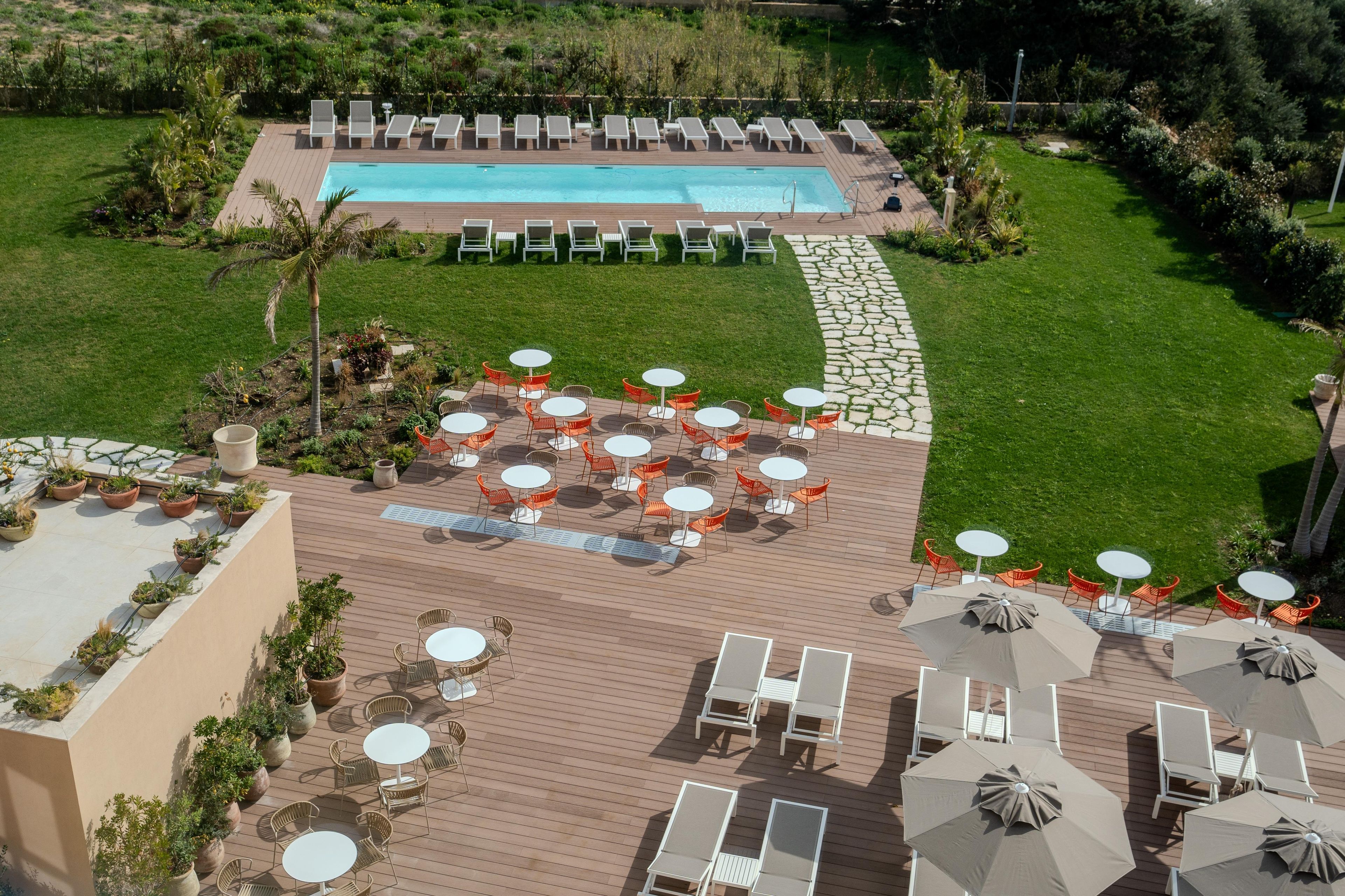 A rooftop pool area with lounge chairs and tables, surrounded by greenery.