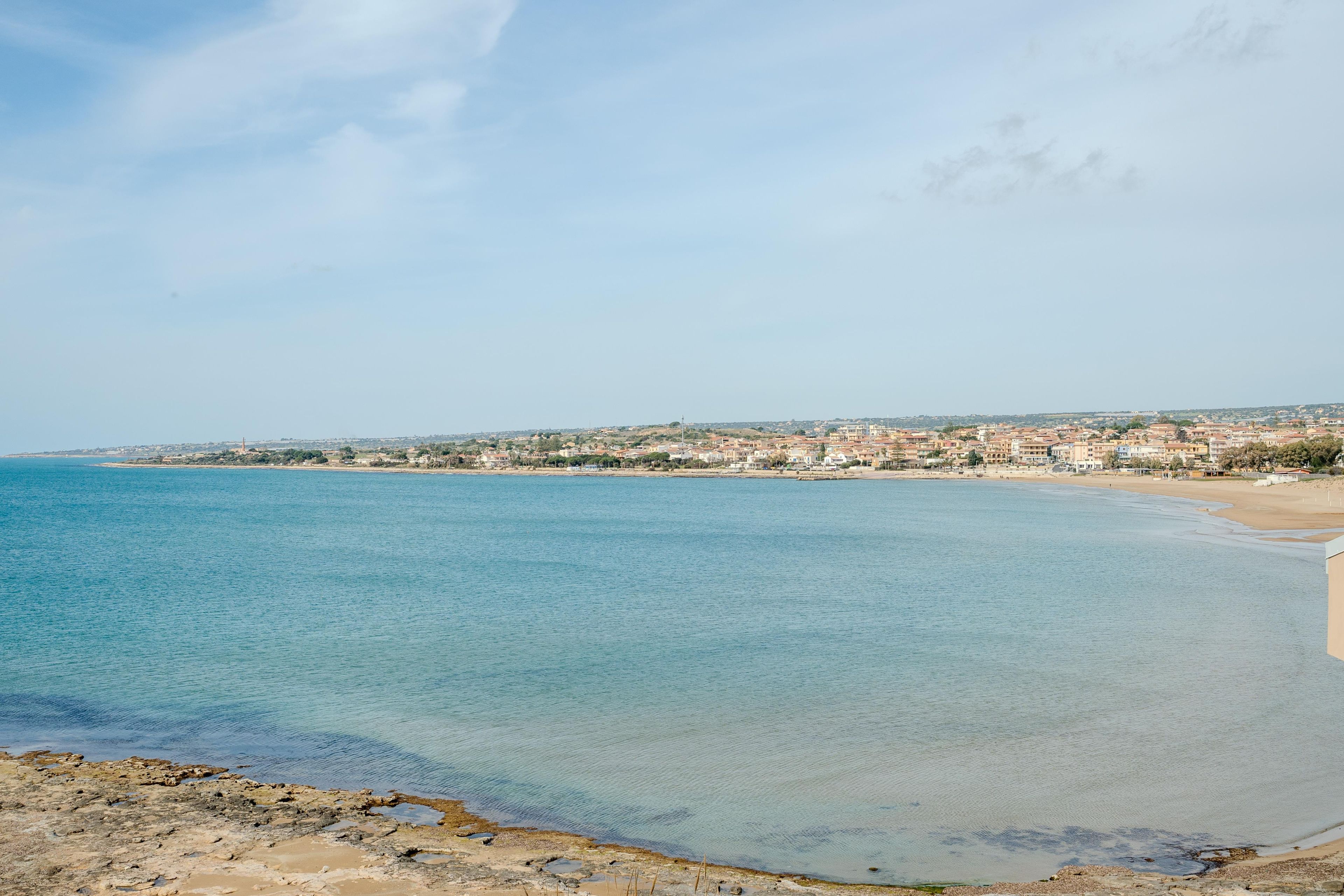 A coastal town with a clear blue sea, sandy beach, and buildings in the distance.