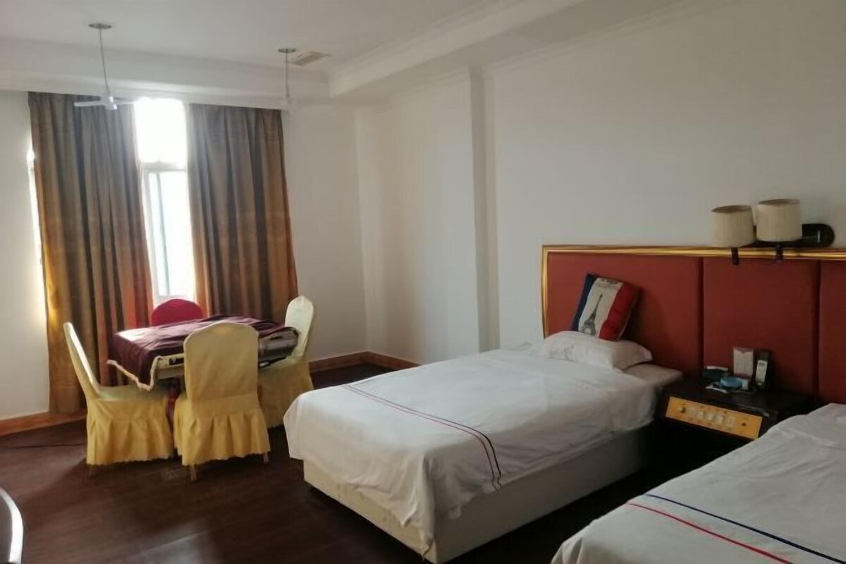 A hotel room with two beds, a desk with a chair, a nightstand, and a window with curtains.