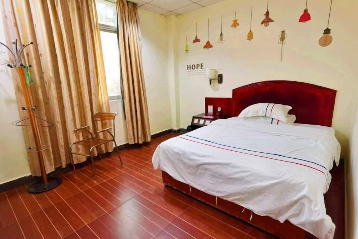 A hotel room with a bed, a nightstand, a lamp, a chair, and a window with curtains.