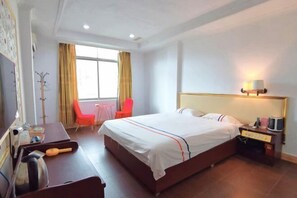 A hotel room with a large bed, a desk with a kettle, a chair, and a small table with a lamp. - Xinhui Hotel (Guangzhou)