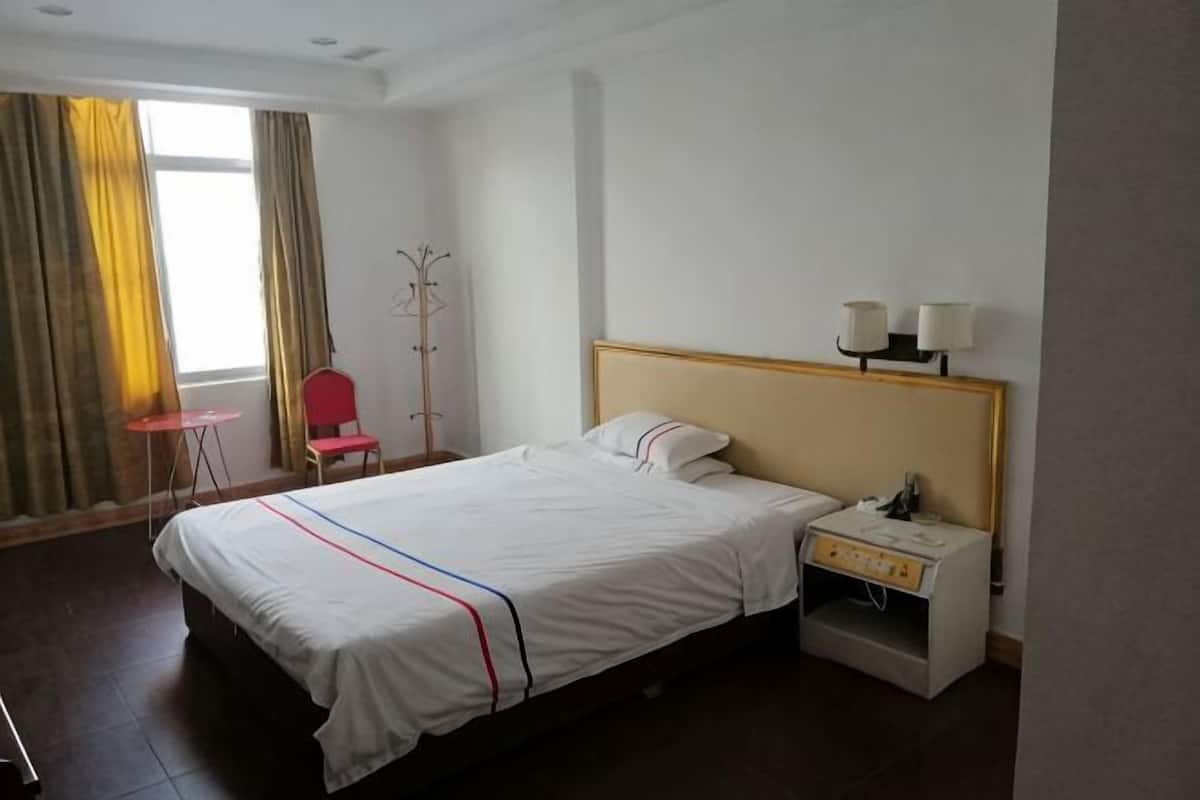 A hotel room with a bed, bedside table, lamp, chair, and a window with curtains.