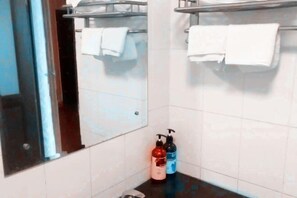 A bathroom with white tiled walls, a mirror, a towel rack, and two bottles of toiletries on the counter. - Xinhui Hotel (Guangzhou)