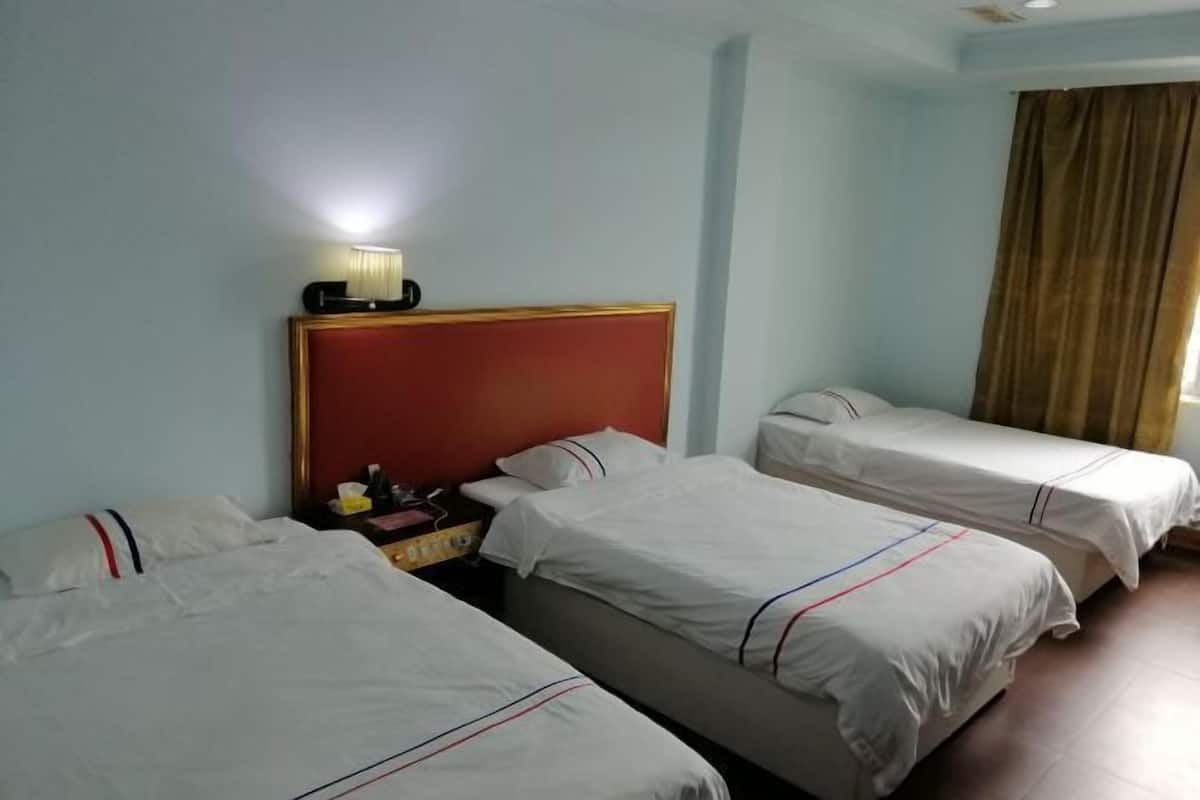 A hotel room with three single beds, a nightstand with a lamp, and a window with curtains.