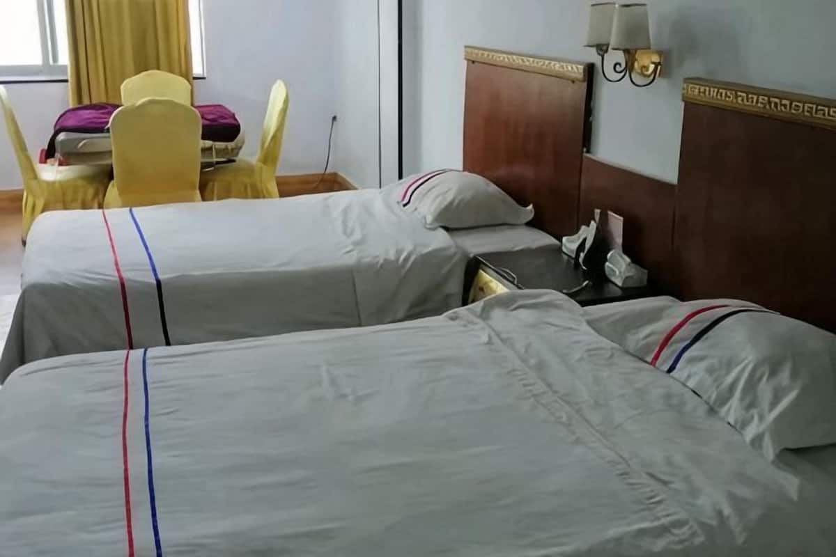 Two beds with white bedding and red stripes, a wooden headboard, a table with chairs, and a lamp on the wall.