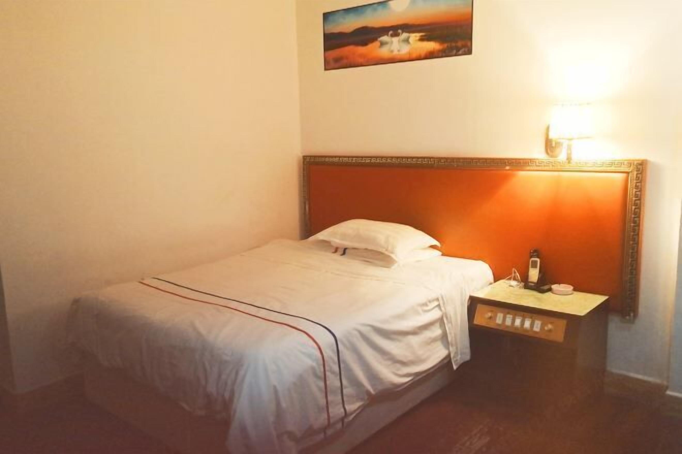 Un lit simple avec une tête de lit en bois, une table de chevet avec une lampe et un tableau accroché au mur.