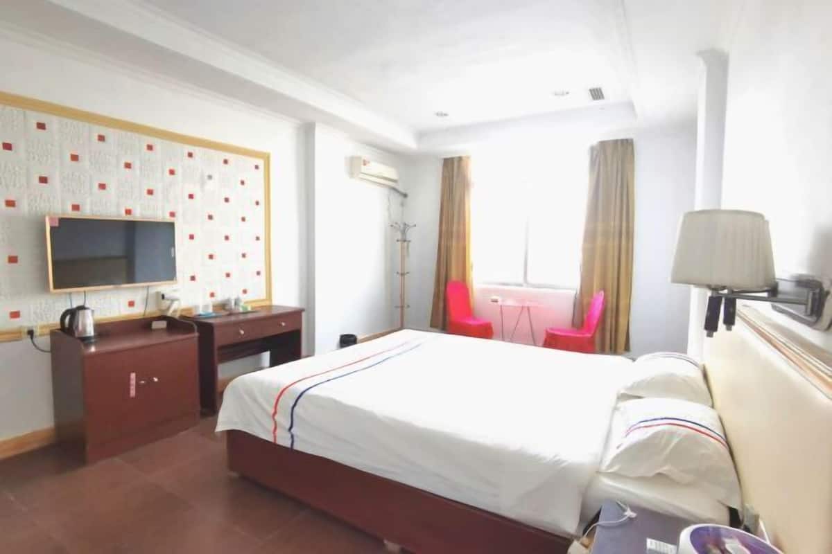 A hotel room with a bed, a desk, a chair, a television, and a window with curtains.