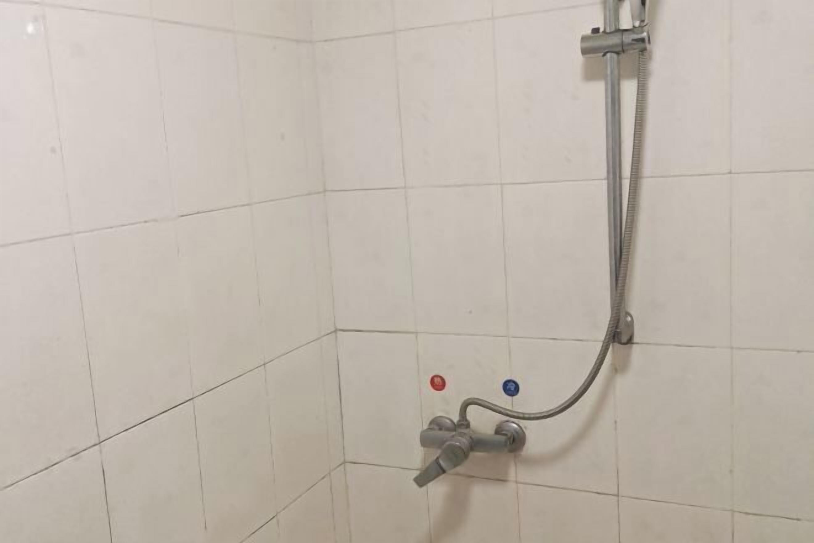 A shower area with white tiled walls and a handheld showerhead.