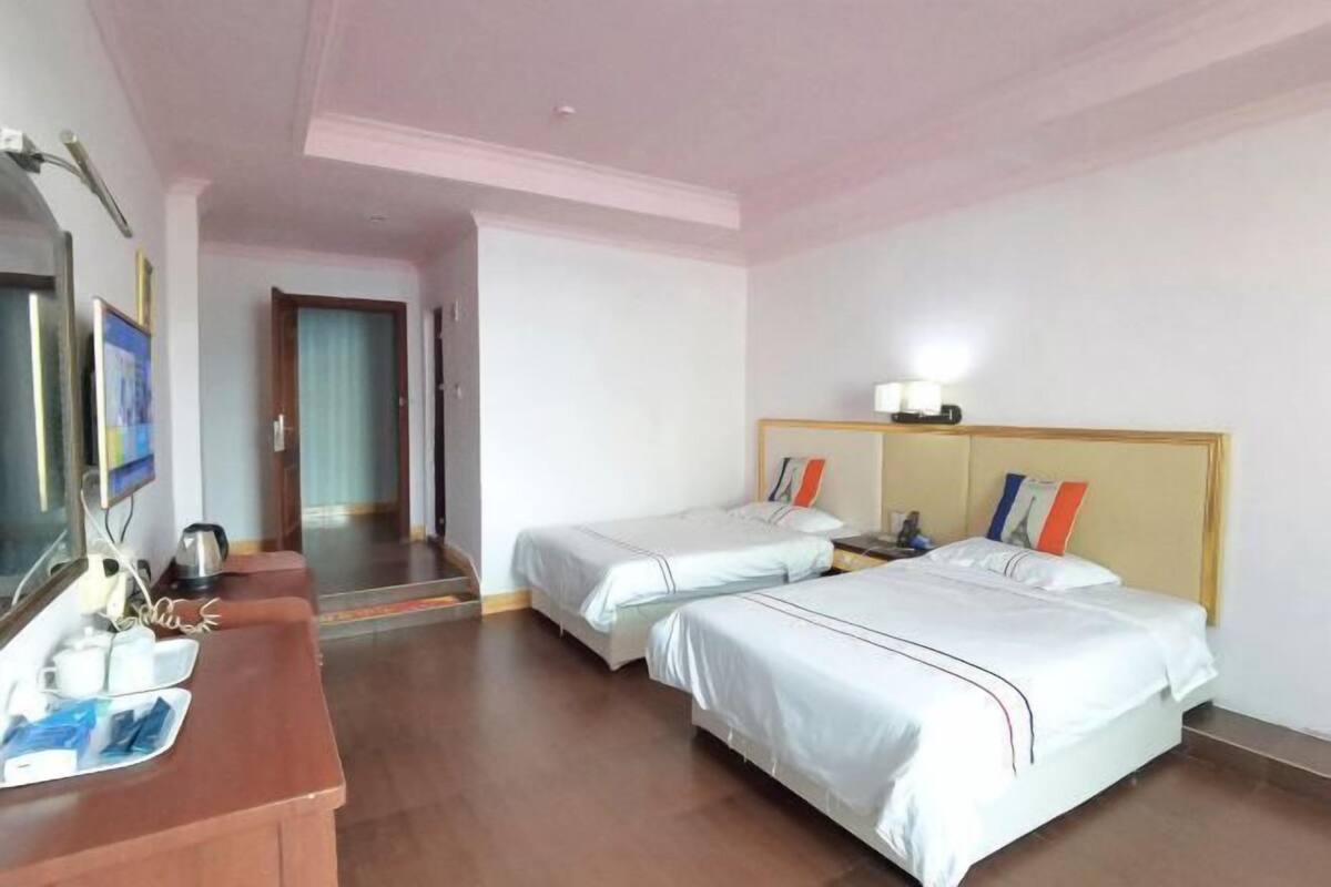 A hotel room with two beds, a wooden desk with a mirror, a nightstand, and a lamp.
