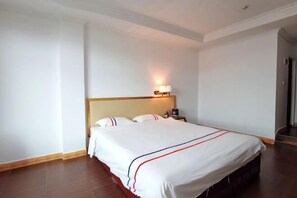 A hotel room with a bed, a nightstand, and a wall-mounted lamp. - Xinhui Hotel (Guangzhou)