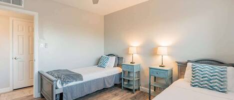A bedroom with two single beds, a ceiling fan, bedside tables with lamps, and a door.