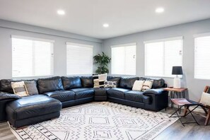 A modern living room with a black leather sectional sofa, a patterned rug, and a small side table with a lamp. - Family Cabin w/games & fire-pit (Payson)