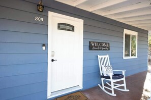 A house with a white door, a welcome sign, and a rocking chair on the porch.