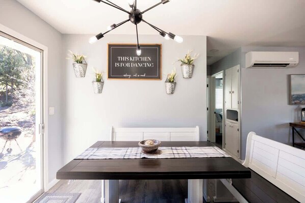 A modern kitchen with a dining table, pendant lighting, and decorative potted plants.