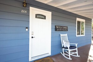 A house with a white door, a welcome sign, and a rocking chair outside.