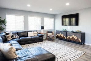 A modern living room with a leather sofa, a patterned rug, a cabinet with geometric designs, and a flat-screen TV mounted on the wall. - Family Cabin Games & Fire Pit (Payson)