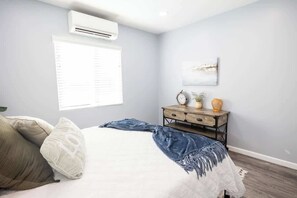 A bedroom with a bed, a nightstand, a wall-mounted air conditioner, a window with blinds, and a wall-mounted clock. - Family Cabin Games & Fire Pit (Payson)