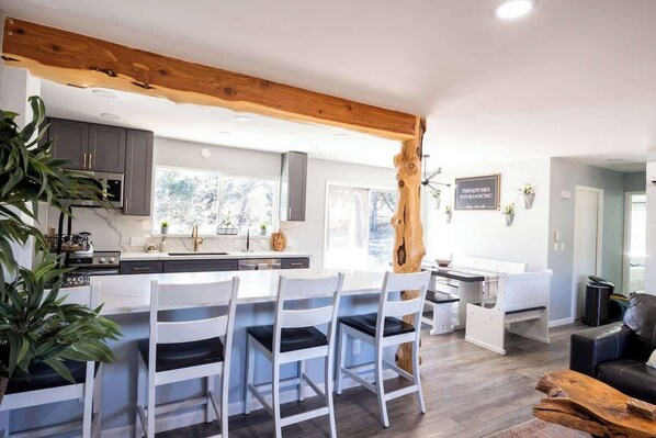 A modern kitchen with white cabinetry, a central island with bar stools, and a wooden beam ceiling. - Family Cabin Games & Fire Pit (Payson)