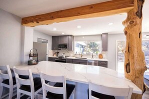 A modern kitchen with a large island, white chairs, and a wooden beam ceiling. - Family Cabin Games & Fire Pit (Payson)
