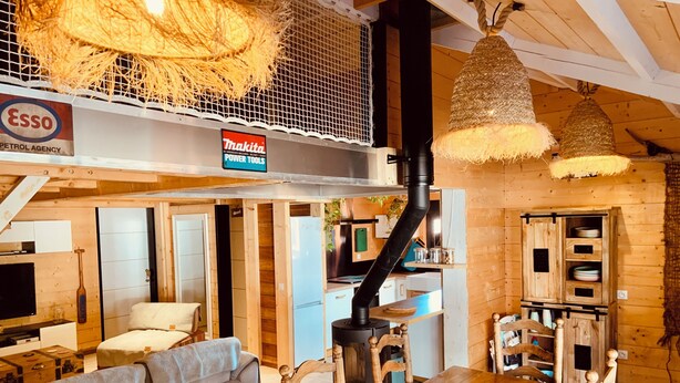 En mysig stuga med en matplats, en soffa, ett kök och en övre våning med en hängande lampa.