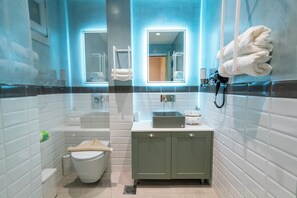 Un baño moderno con un inodoro blanco, un lavamanos con espejo y un perchero con toallas.