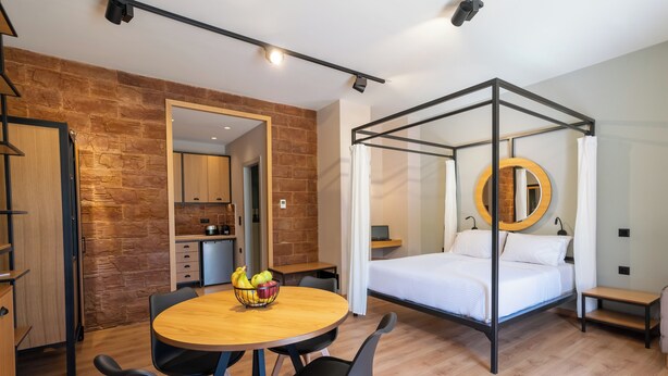 A modern bedroom with a four-poster bed, a round mirror, and a dining area with a table and chairs.