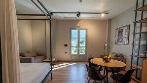 A modern room with a bed, a dining table with chairs, a small kitchen area, and a balcony with a view of the mountains.