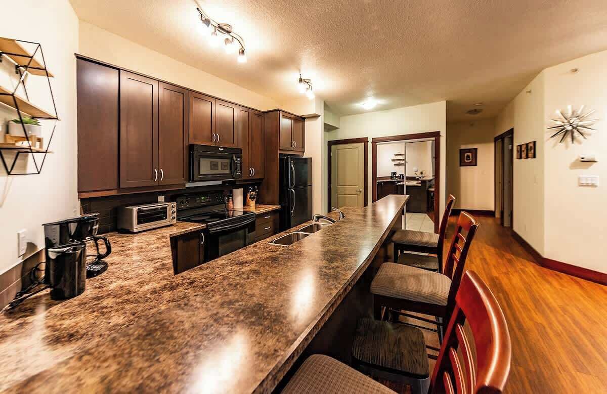 A modern kitchen with dark wooden cabinets, a granite countertop, and a built-in microwave.