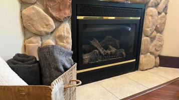 A fireplace with a stone wall, a basket with towels, and a wooden floor.