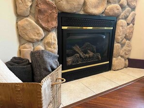 A fireplace with a stone wall, a basket with towels, and a wooden floor. - Pool, Hot Tub & Gym | Near Fernie Alpine Resort (Fernie)