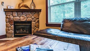 A stone fireplace with a mantel, a leather sofa, and a wooden coffee table with magazines. - Pool, Hot Tub & Gym | Near Fernie Alpine Resort (Fernie)