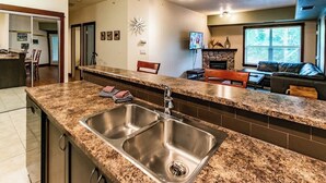 A kitchen with granite countertops, stainless steel sink, and a stone fireplace. - Pool, Hot Tub & Gym | Near Fernie Alpine Resort (Fernie)
